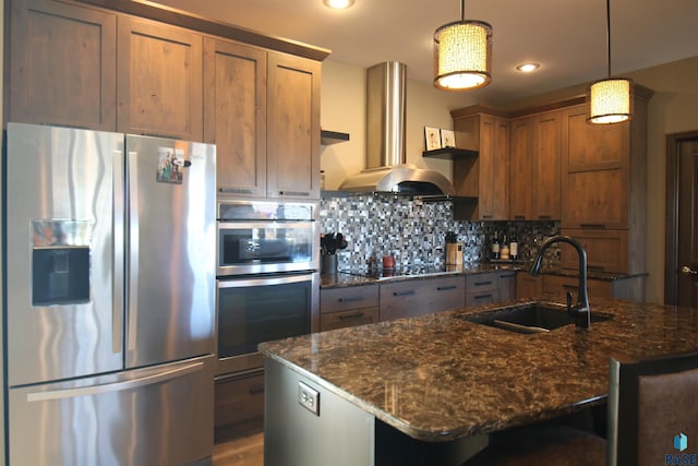 kitchen with extractor fan, stainless steel appliances, a sink, hanging light fixtures, and a center island with sink