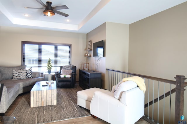 living room with ceiling fan, wood-type flooring, and a tray ceiling