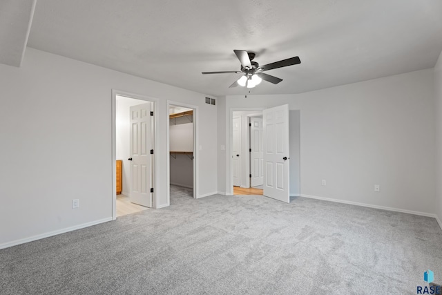 unfurnished bedroom featuring a spacious closet, ceiling fan, ensuite bathroom, light colored carpet, and a closet