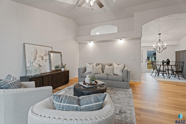 living room featuring lofted ceiling, light wood-type flooring, and ceiling fan with notable chandelier