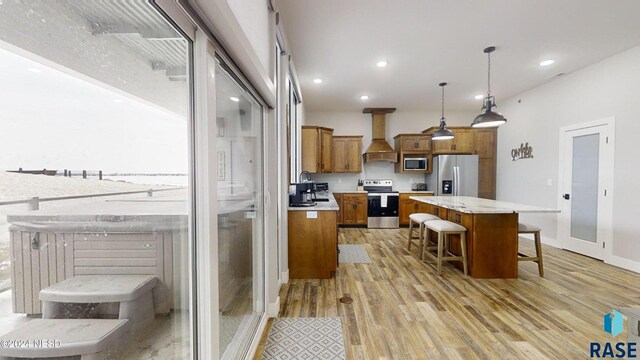 kitchen featuring pendant lighting, a center island, appliances with stainless steel finishes, light hardwood / wood-style floors, and custom range hood