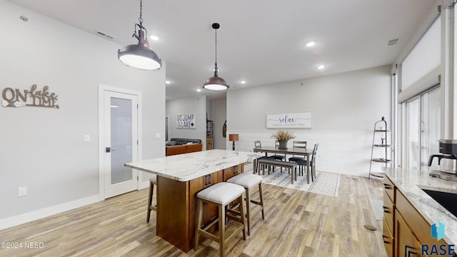 kitchen featuring light stone countertops, a center island, a kitchen breakfast bar, light hardwood / wood-style flooring, and pendant lighting