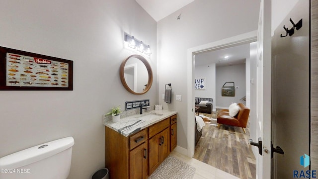 bathroom with toilet, vanity, vaulted ceiling, and hardwood / wood-style flooring