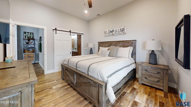 bedroom with a closet, a barn door, ceiling fan, and light hardwood / wood-style flooring