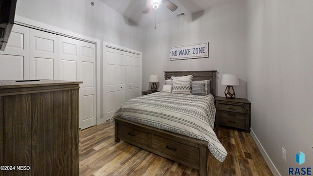 bedroom with vaulted ceiling, ceiling fan, dark wood-type flooring, and two closets