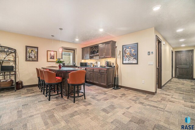 interior space featuring dark brown cabinetry, hanging light fixtures, a kitchen breakfast bar, light colored carpet, and a kitchen island