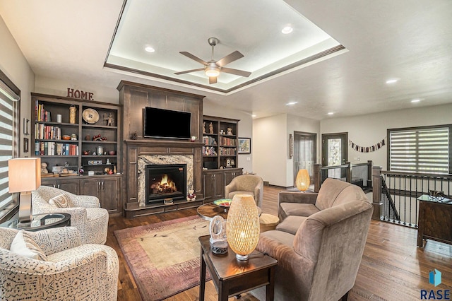 living room featuring a tray ceiling, a premium fireplace, dark hardwood / wood-style flooring, and ceiling fan