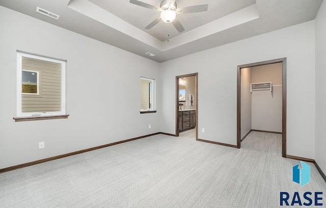 unfurnished bedroom featuring a spacious closet, light carpet, a tray ceiling, and ensuite bath