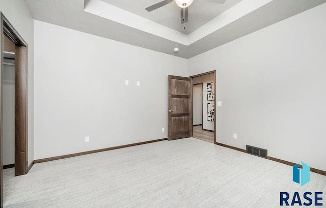 unfurnished bedroom featuring light colored carpet, ceiling fan, and a tray ceiling