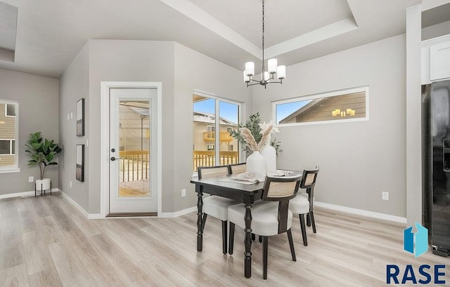 dining area featuring a notable chandelier, light hardwood / wood-style floors, and a tray ceiling