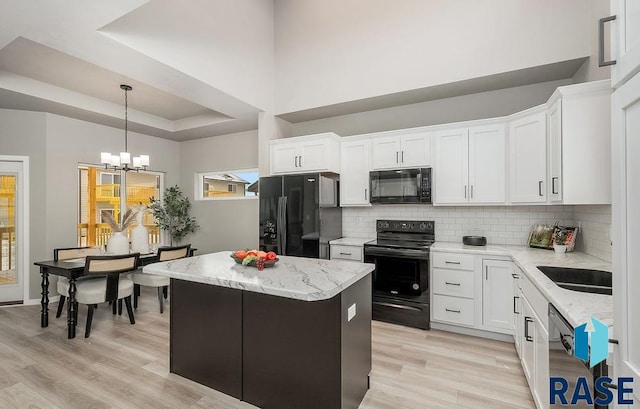 kitchen with a center island, black appliances, white cabinets, light wood-type flooring, and a notable chandelier