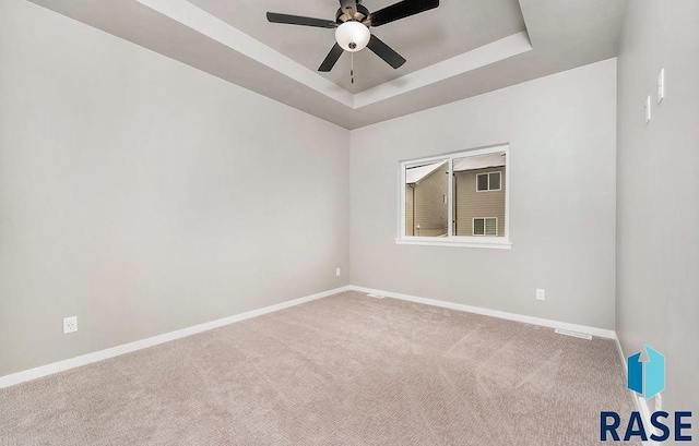 empty room with carpet, a tray ceiling, and ceiling fan