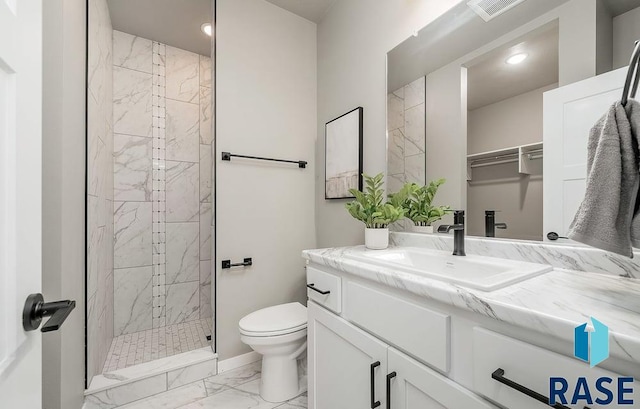 bathroom with a tile shower, vanity, and toilet