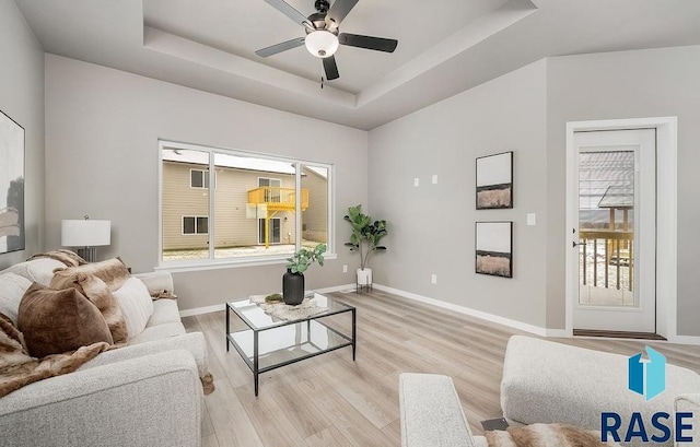 living room with a raised ceiling and light wood-type flooring