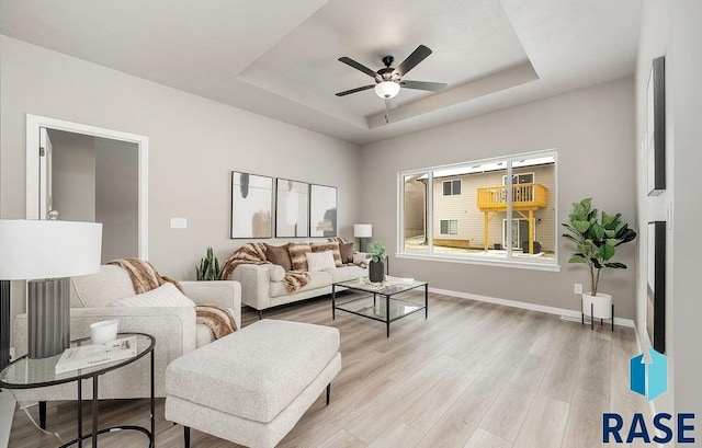 living room with ceiling fan, light hardwood / wood-style floors, and a raised ceiling