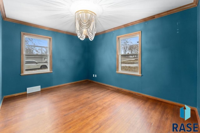 empty room featuring wood-type flooring, ornamental molding, a healthy amount of sunlight, and a notable chandelier