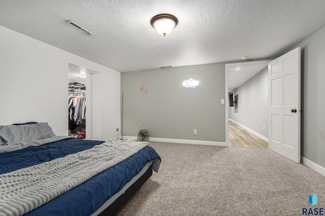 bedroom with light carpet, a textured ceiling, a closet, and a walk in closet