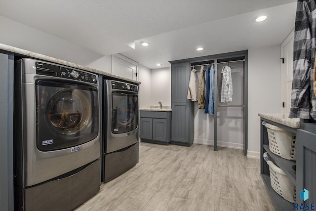 clothes washing area featuring cabinets, light hardwood / wood-style flooring, washer and dryer, and sink