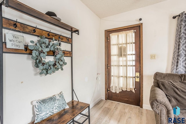 doorway with vaulted ceiling, plenty of natural light, a textured ceiling, and light hardwood / wood-style floors