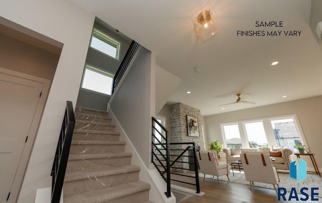 stairs with hardwood / wood-style floors, ceiling fan, and a brick fireplace