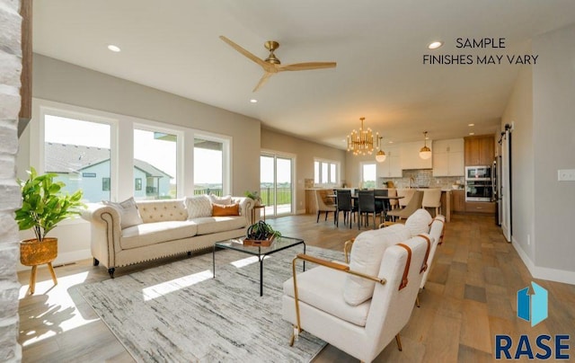 living room with ceiling fan with notable chandelier and light hardwood / wood-style floors