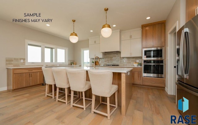 kitchen with stainless steel appliances, pendant lighting, light hardwood / wood-style floors, a center island with sink, and white cabinets