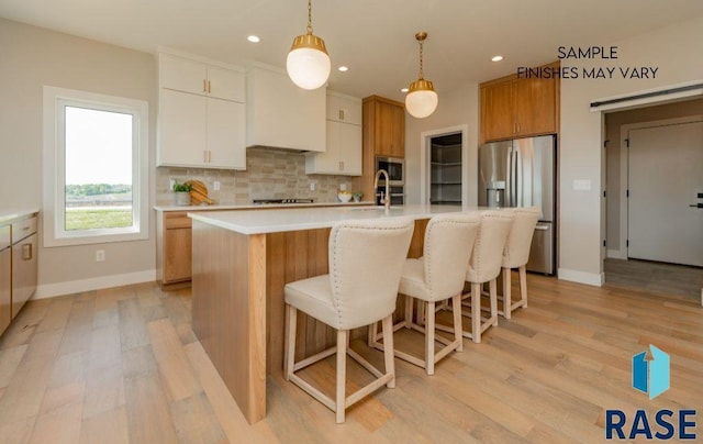 kitchen with white cabinetry, light hardwood / wood-style flooring, an island with sink, decorative light fixtures, and appliances with stainless steel finishes