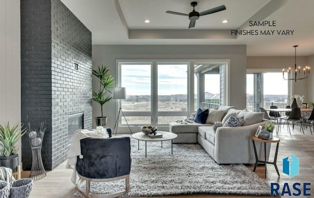 living room with a large fireplace, hardwood / wood-style floors, and ceiling fan with notable chandelier