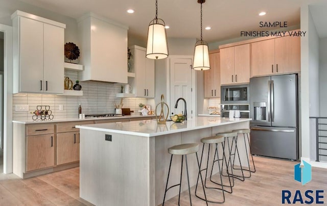 kitchen featuring pendant lighting, backsplash, an island with sink, light hardwood / wood-style floors, and stainless steel appliances