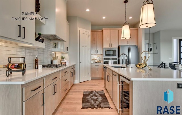 kitchen with a large island, light brown cabinets, hanging light fixtures, wall chimney range hood, and light hardwood / wood-style floors