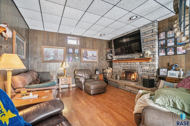 living room featuring hardwood / wood-style floors, a drop ceiling, wood walls, and a fireplace