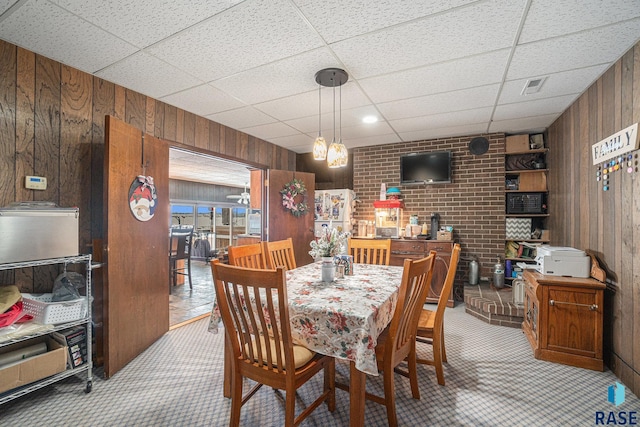 dining space with a drop ceiling, wood walls, and light colored carpet