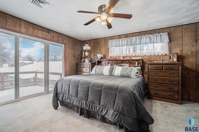 bedroom featuring ceiling fan, wood walls, access to exterior, and light carpet