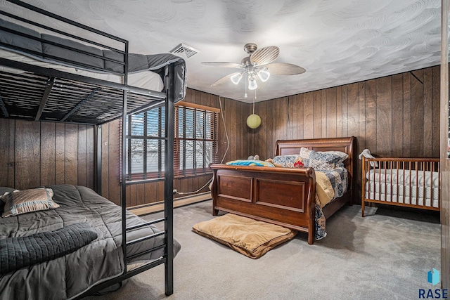 bedroom featuring carpet flooring, a baseboard radiator, ceiling fan, and wood walls