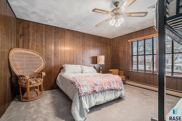 carpeted bedroom with baseboard heating, ceiling fan, and wooden walls