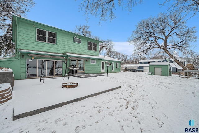 snow covered house with a storage shed and an outdoor fire pit