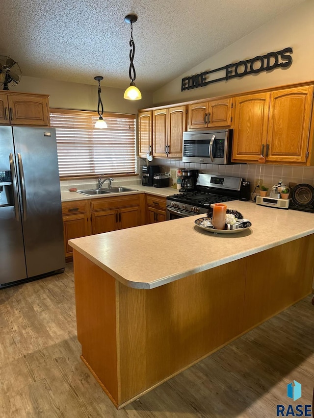 kitchen with sink, vaulted ceiling, appliances with stainless steel finishes, decorative light fixtures, and light hardwood / wood-style floors