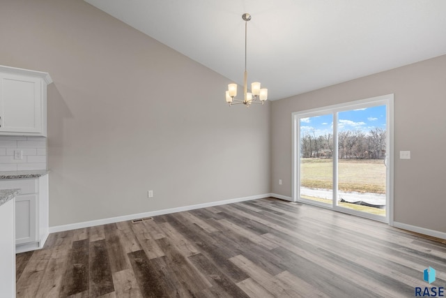 unfurnished dining area featuring light hardwood / wood-style floors, lofted ceiling, and a notable chandelier