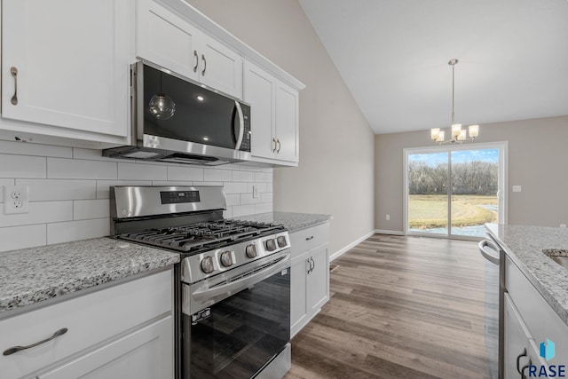 kitchen featuring backsplash, a chandelier, lofted ceiling, white cabinets, and appliances with stainless steel finishes