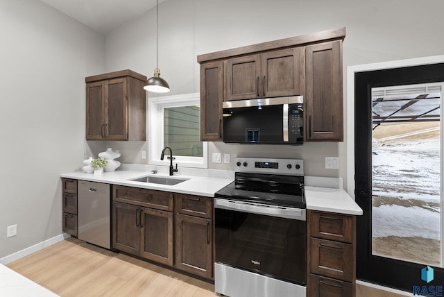 kitchen with appliances with stainless steel finishes, dark brown cabinetry, sink, light hardwood / wood-style flooring, and hanging light fixtures