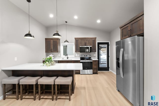 kitchen featuring decorative light fixtures, dark brown cabinetry, a breakfast bar area, and appliances with stainless steel finishes