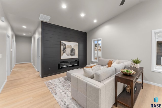 living room with ceiling fan, light hardwood / wood-style floors, a fireplace, and vaulted ceiling