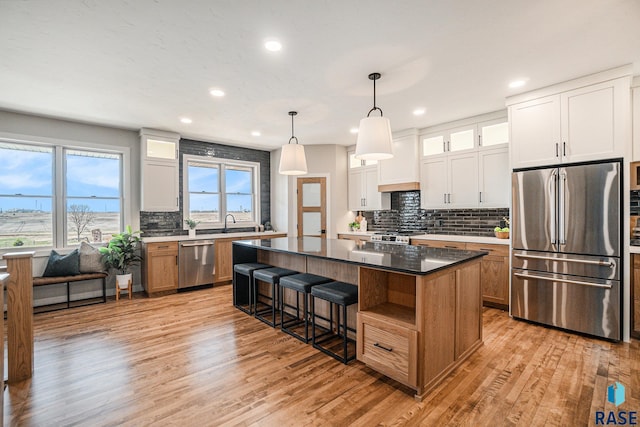 kitchen featuring stainless steel appliances, white cabinetry, light hardwood / wood-style flooring, a kitchen island, and hanging light fixtures