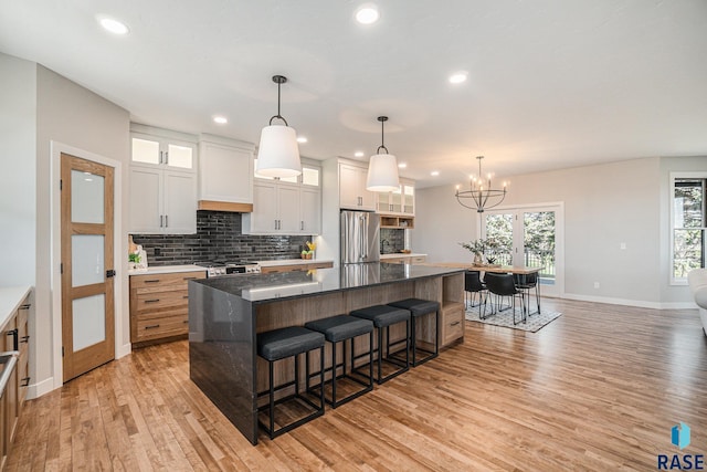 kitchen featuring white cabinets, stainless steel fridge, decorative light fixtures, and a large island