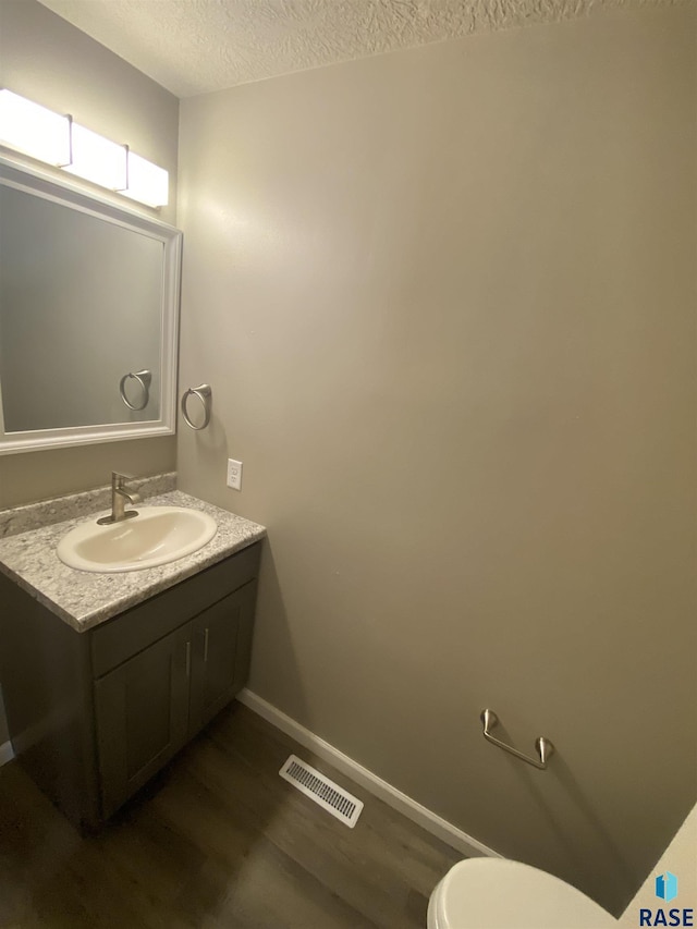 bathroom with toilet, vanity, a textured ceiling, and hardwood / wood-style flooring