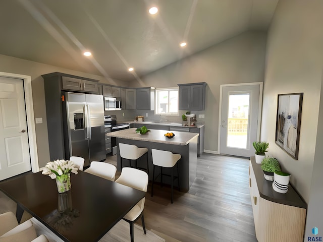 kitchen with gray cabinetry, a center island, high vaulted ceiling, hardwood / wood-style flooring, and stainless steel appliances