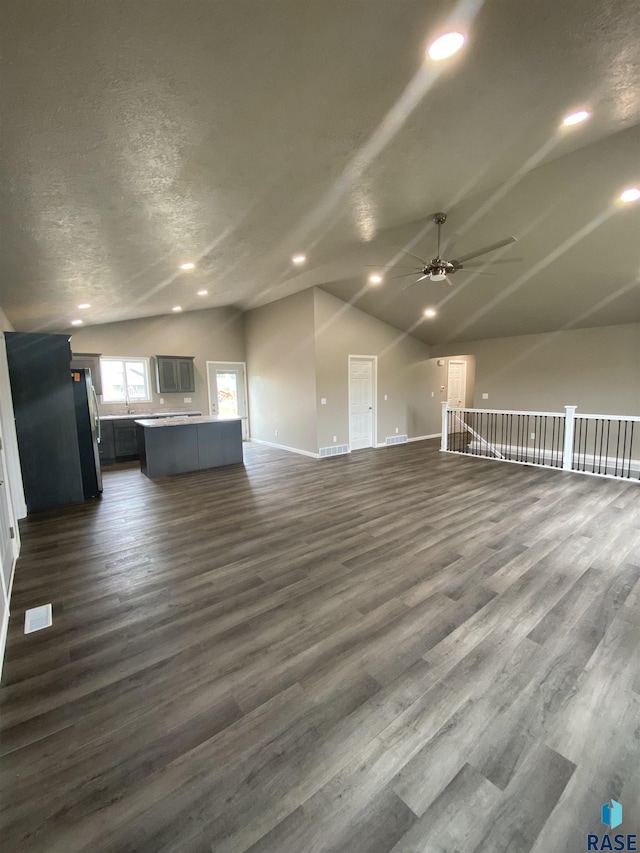 unfurnished living room with ceiling fan, dark hardwood / wood-style flooring, lofted ceiling, and a textured ceiling