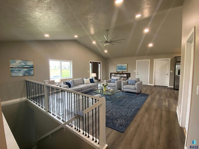 living room featuring vaulted ceiling, ceiling fan, dark wood-type flooring, and a textured ceiling