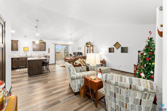 living room featuring a notable chandelier, sink, vaulted ceiling, and light hardwood / wood-style flooring