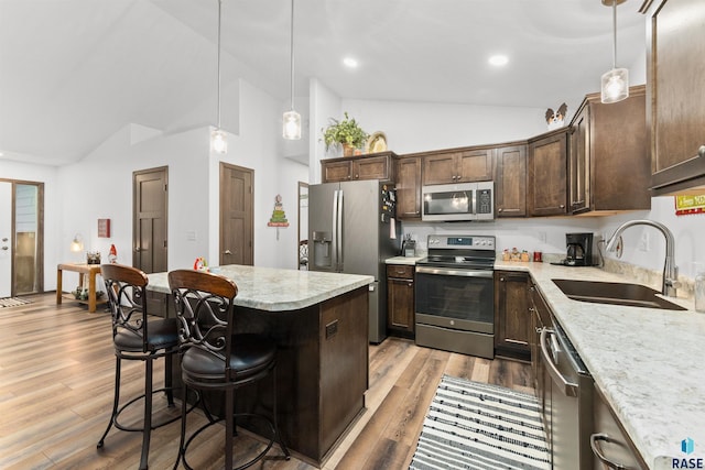 kitchen featuring light stone counters, dark brown cabinetry, stainless steel appliances, sink, and pendant lighting